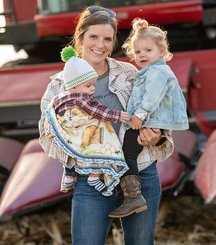 Mom with two young kids and farm equipment in the background.