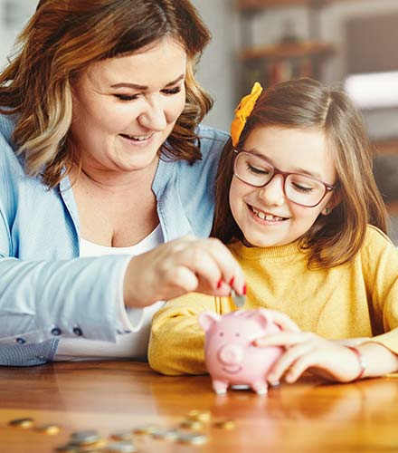 Mom and girl putting coins in a piggy bank.