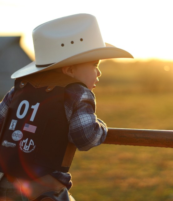 a young boy in a cowboy hat and riding vest