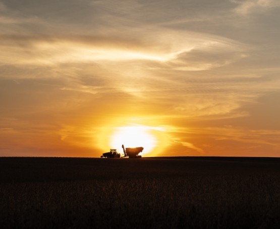 The sun sets over the horizon silhouetting a tractor pulling equipment