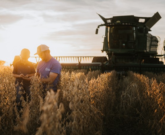 a farmer and his son stand in a wheat field with the combine behind them