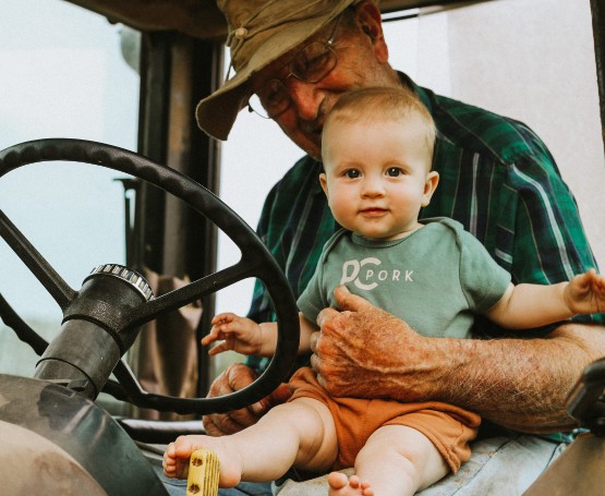A grandfather holds his new born grandchild while sitting in a tractor